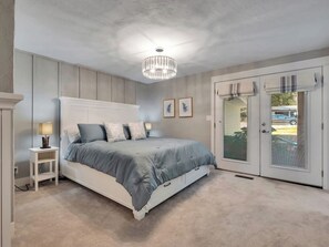 Une chambre à coucher comprenant un lit, des tables de chevet, un lustre et une porte-fenêtre coulissante donnant sur l’extérieur.