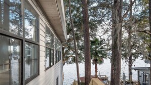Une terrasse en bois mène à un bâtiment blanc doté de grandes fenêtres donnant sur une étendue d’eau.