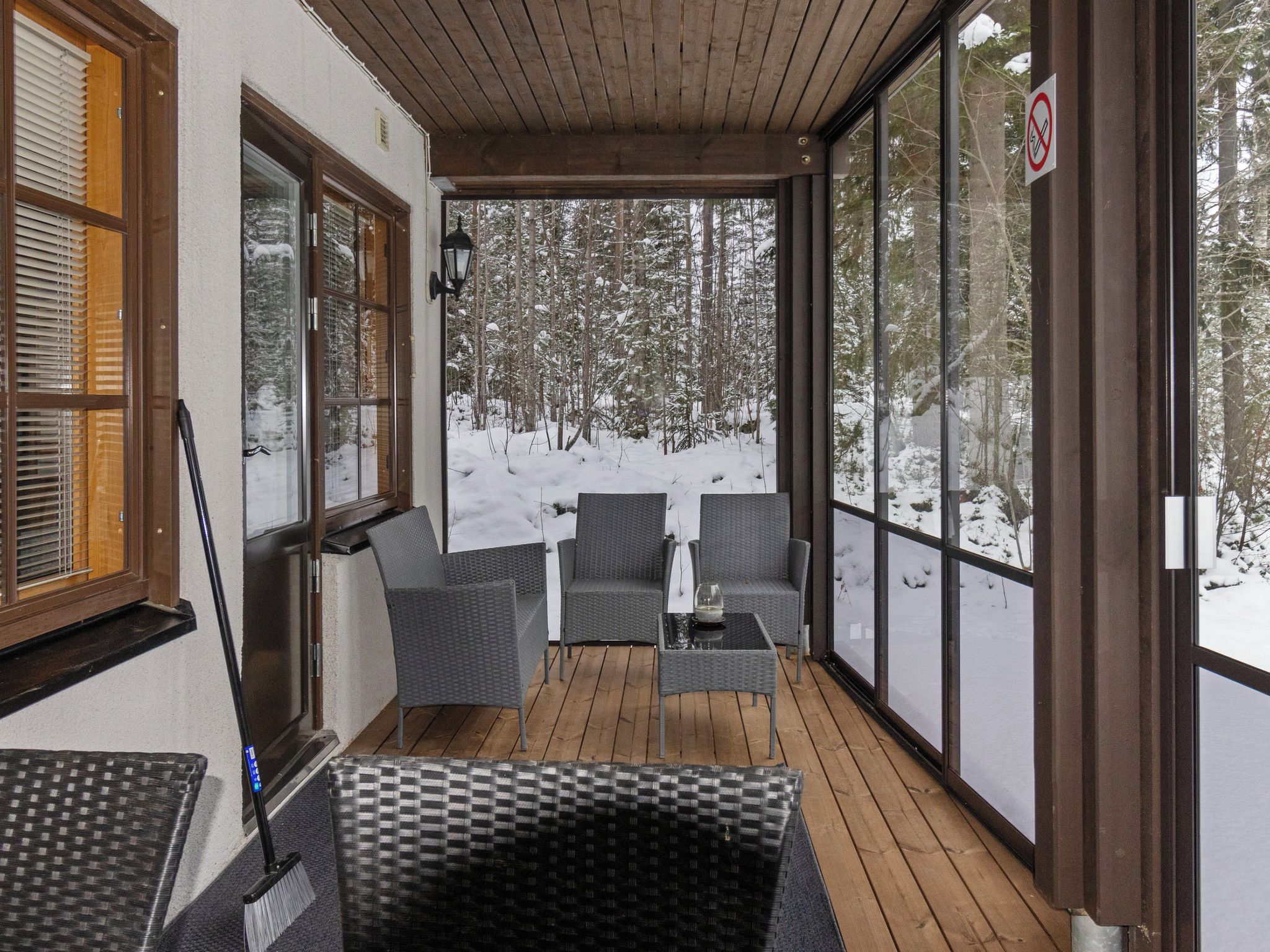 Een overdekt terras met rieten meubels, een glazen tafel en uitzicht op een besneeuwd bos.