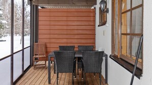 Een overdekt terras met een tafel, stoelen en een houten bank, plus een raam met zonwering.