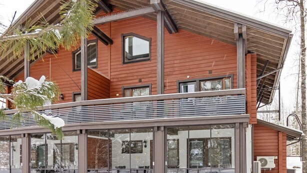 Een modern gebouw met een houten gevel, grote ramen en een overdekt balkon.