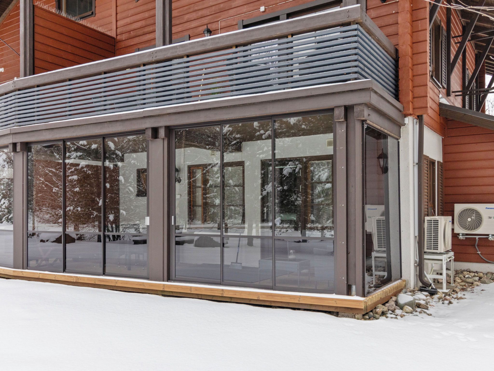 A glass-enclosed structure with a metal roof, adjacent to a building with wooden siding.