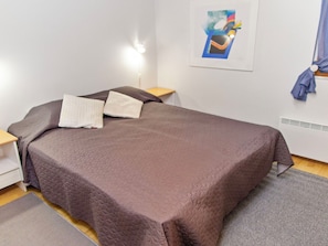 A bedroom with a bed, a nightstand, a lamp, a wall art piece, and a window with curtains. - Alppitalo sinitähti 9 as 1 by Interhome (Nilsiä)