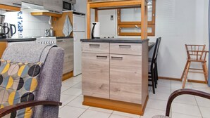Een moderne keuken met houten kastjes, een magnetron en een koffieapparaat. Er is een eethoek met een stoel en een tafel.