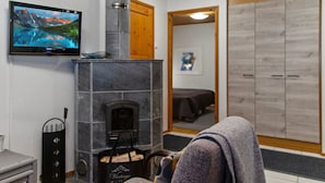 Een knus vertrek met een stenen openhaard, een aan de muur bevestigde televisie en een houten plafond.