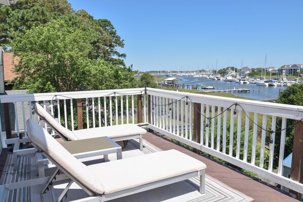 A deck with lounge chairs and a table overlooking a marina with boats.