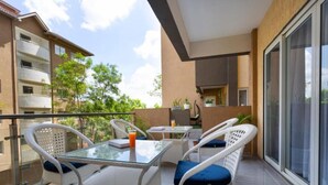 Un balcon avec une table en verre, des chaises en osier blanc et une vue sur la façade de l’immeuble.