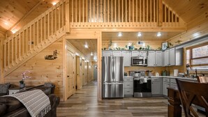 A wooden interior with a kitchen area featuring stainless steel appliances, a dining area with a table and chairs, and a staircase leading to another level.