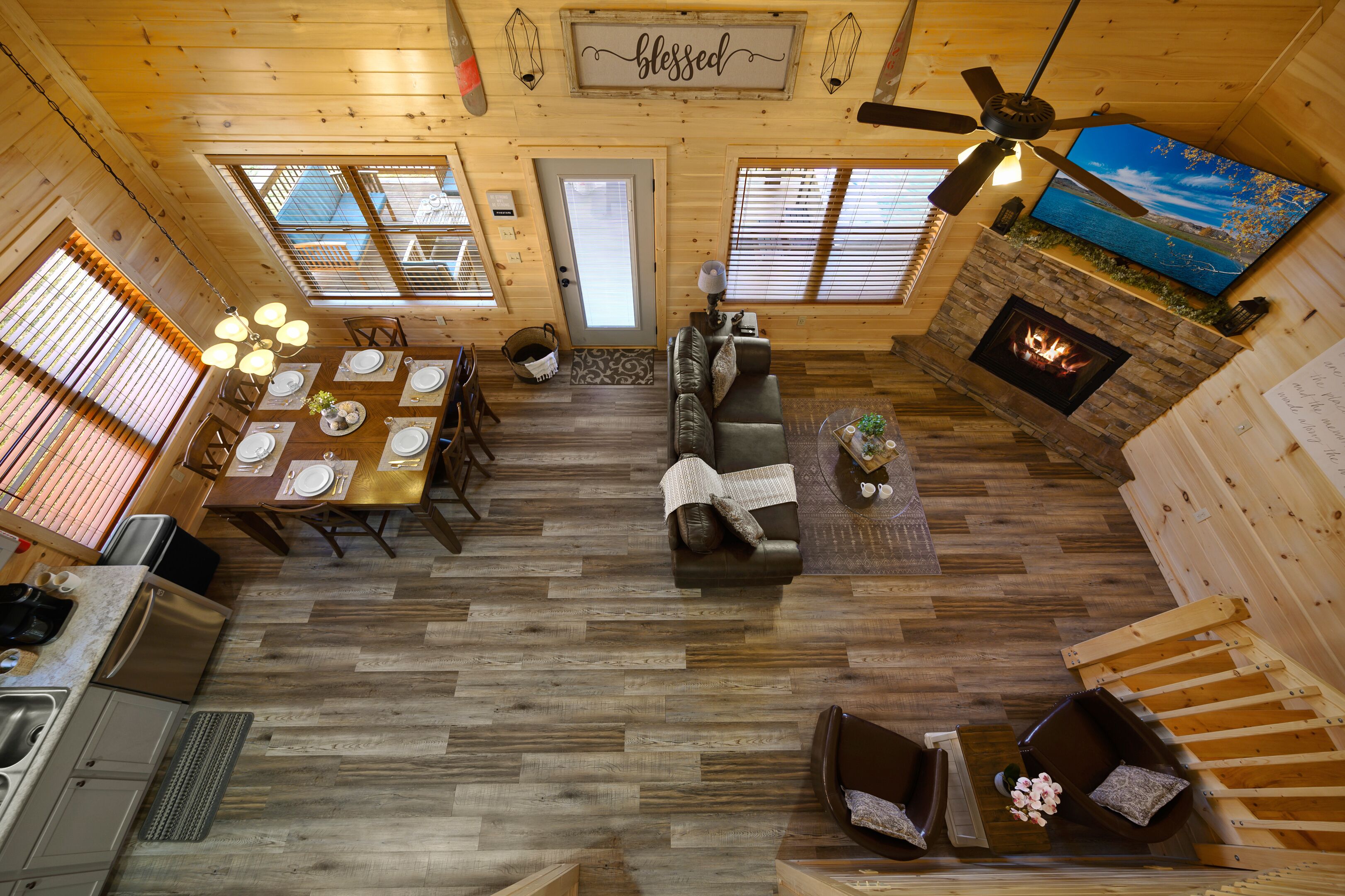A spacious cabin interior with a dining area, living room, fireplace, and a television mounted on the wall.