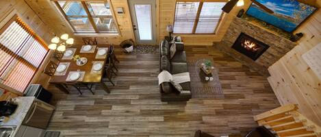 A spacious cabin interior with a dining area, living room, fireplace, and a television mounted on the wall.