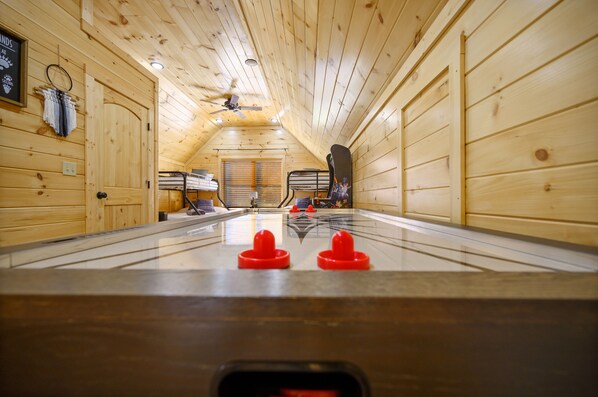 A room with wooden walls and a ceiling fan, featuring a foosball table and a bed with a headboard.