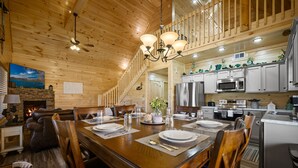 A wooden interior with a dining table set for four, a fireplace, and a kitchen with modern appliances.