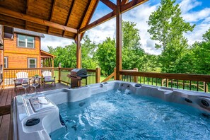 Relax on the deck with a hot tub, table, and barbecue grill, surrounded by a lush landscape.