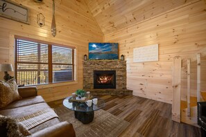 Relax in a warm and inviting space with a cozy seating area, stone fireplace, and large windows offering views of the outdoors.