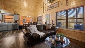 A spacious wooden cabin interior with a living area featuring a leather couch, a glass coffee table, and a dining area with a table and chairs.