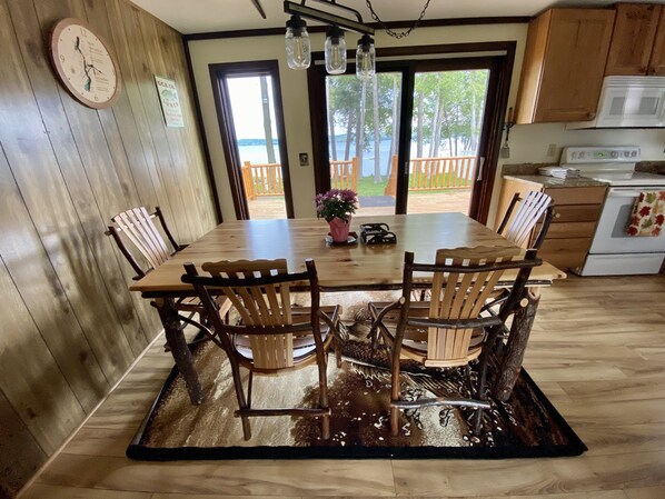 Una mesa de comedor de madera con cuatro sillas, un reloj en la pared y vistas al exterior a través de una puerta.