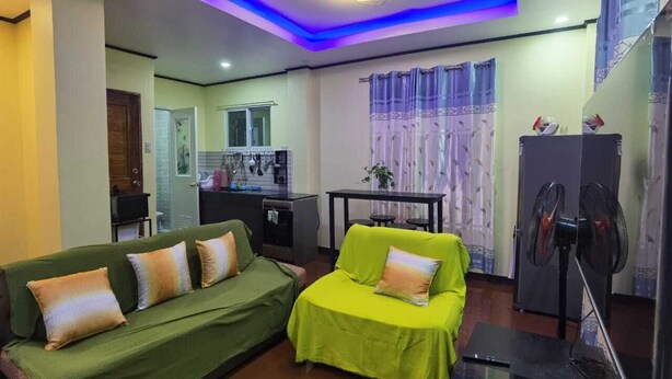 Uma sala de estar com dois sofás verdes, uma mesinha e um ventilador.