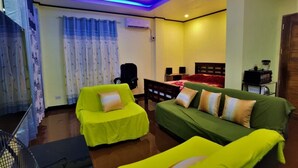 Um quarto com uma cama, dois sofás verdes, uma mesinha e uma cadeira.