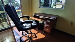 Quarto com escrivaninha, cadeira e janela grande.