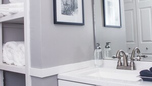 A bathroom with a white vanity, a mirror, and a shelf with towels. - Modern Designer Condo Near I55 w/Balcony (Jackson)