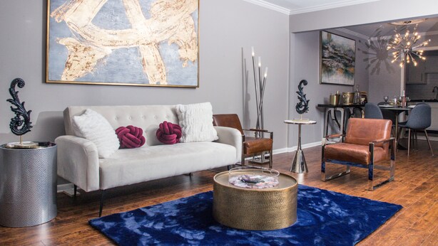 A modern living room with a white sofa, a blue rug, and a large abstract painting. - Modern Designer Condo Near I55 w/Balcony (Jackson)