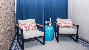 Two armchairs with colorful pillows, a small blue table with a bottle and glasses, and a blue curtain in the background. - Modern Designer Condo Near I55 w/Balcony (Jackson)