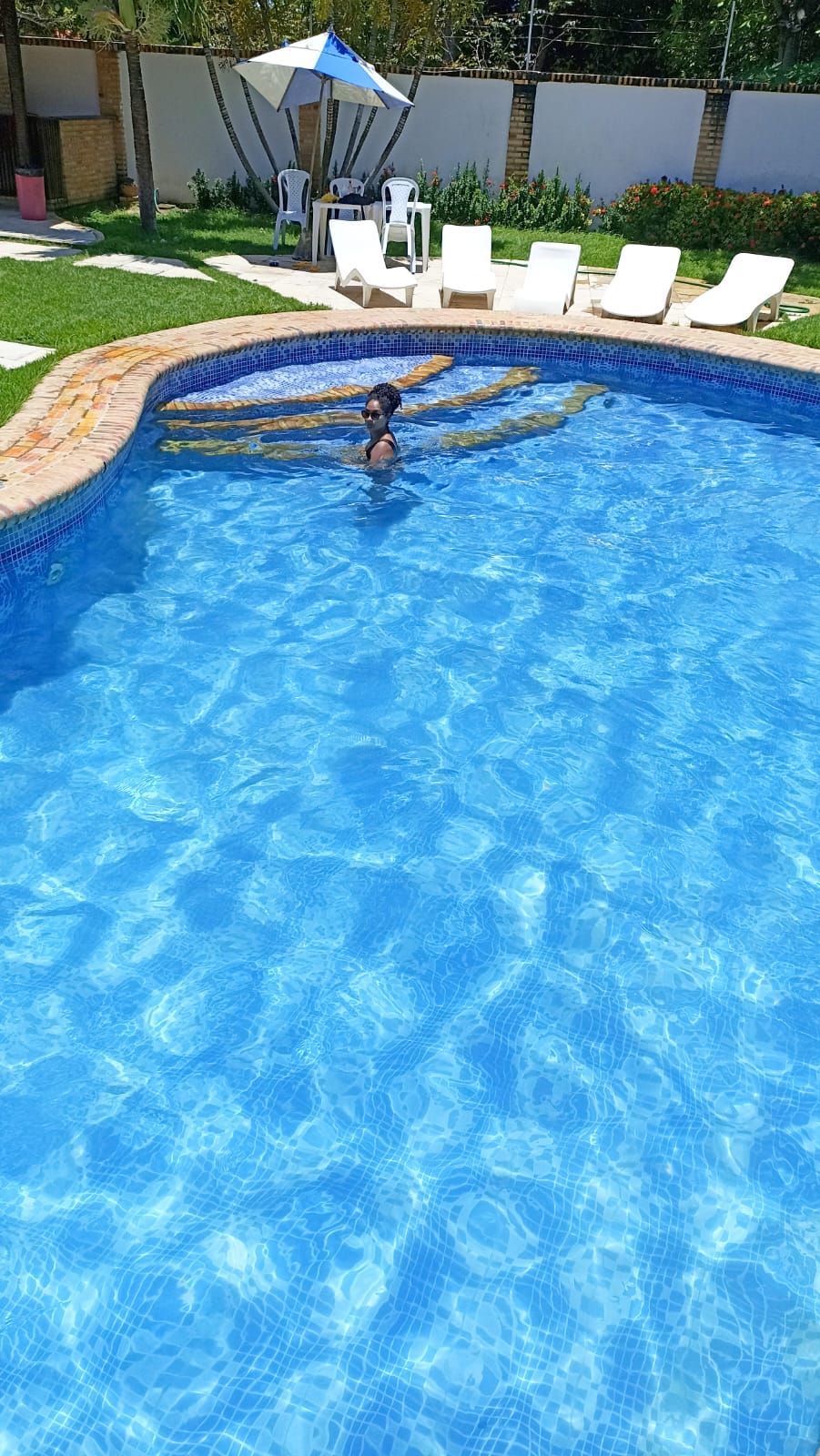 A swimming pool with a tiled edge, surrounded by white lounge chairs and a covered seating area.