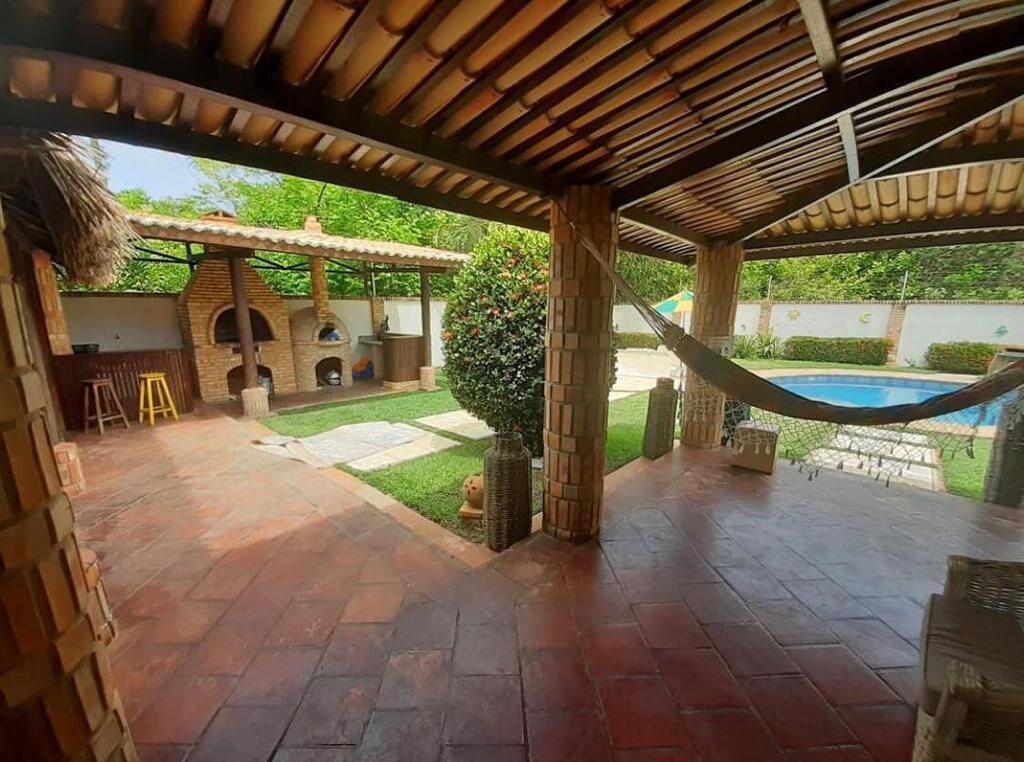 A covered patio area with a brick floor, a hammock, and a pool in the background.