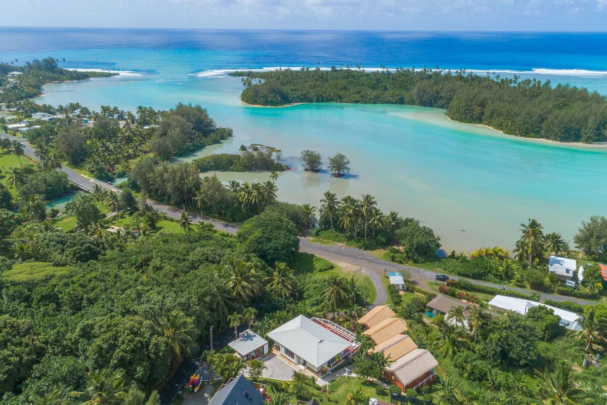 An aerial view of a tropical resort with a beach, clear turquoise waters, and lush greenery.