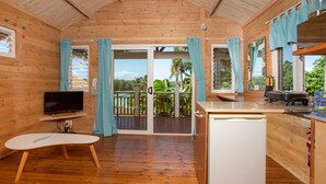 Une cabane en bois comprenant une cuisine, un coin repas et un balcon agrémenté de rideaux.