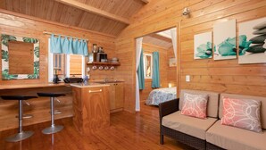 L'intérieur d'un chalet en bois comprend une cuisine, des tabourets de bar, un canapé avec des coussins à motifs et des œuvres d'art accrochées aux murs.