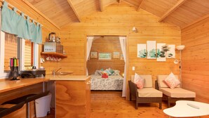 Une cabane en bois chaleureuse comprenant un coin cuisine, une table à manger et une chambre avec deux lits.
