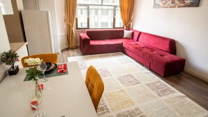 Un salon moderne avec un canapé rouge, une table à manger avec des chaises et une grande fenêtre avec des rideaux.