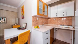 Une cuisine moderne avec des armoires blanches, un évier et un plan de travail. On y trouve une table à manger avec une chaise, et un panier de fruits posé sur le plan de travail.