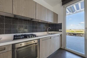 A modern kitchen with a gas stove, stainless steel appliances, and a large window with a view of the outdoors.