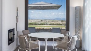 Een kamer met een ronde tafel en vier stoelen, een groot raam met uitzicht op een landschap en een decoratieve kolom.