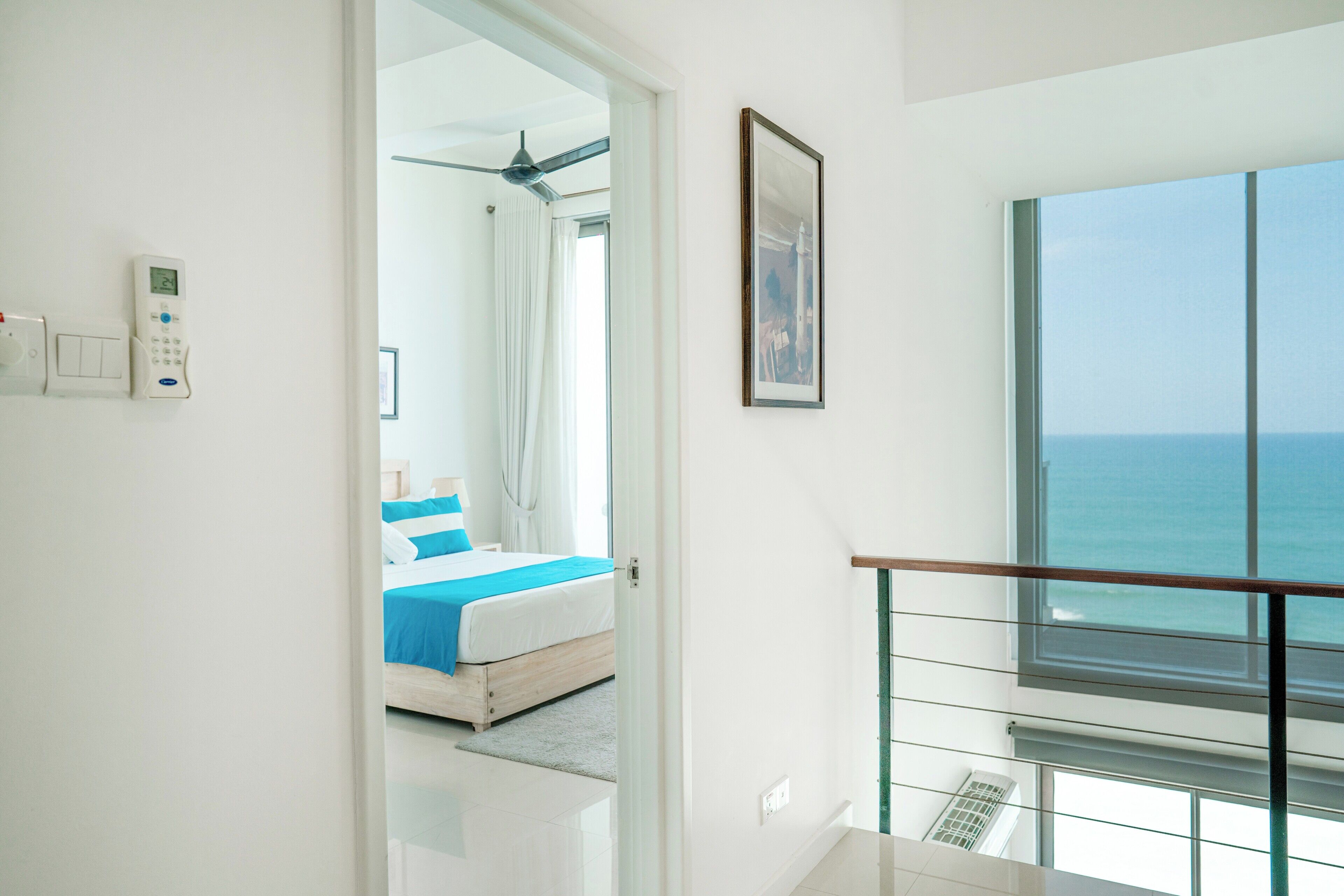Ein modernes Hotelzimmer mit Balkon, einem Bett mit blauer Bettwäsche, einem Deckenventilator und Meerblick.