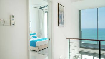 Ein modernes Hotelzimmer mit Balkon, einem Bett mit blauer Bettwäsche, einem Deckenventilator und Meerblick.