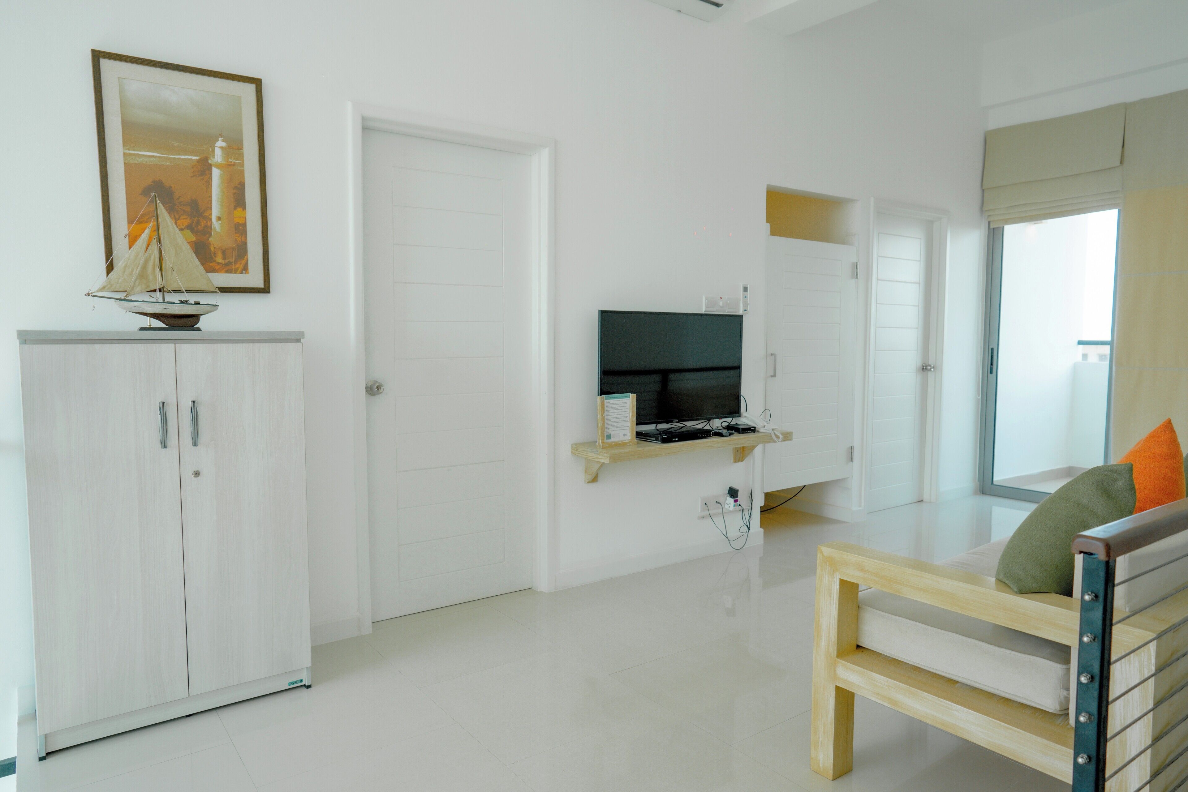 Un soggiorno minimalista con un armadietto bianco, una TV a schermo piatto su un supporto in legno, una panca di legno con cuscini e un quadro appeso al muro.