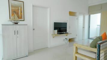 Un soggiorno minimalista con un armadietto bianco, una TV a schermo piatto su un supporto in legno, una panca di legno con cuscini e un quadro appeso al muro.