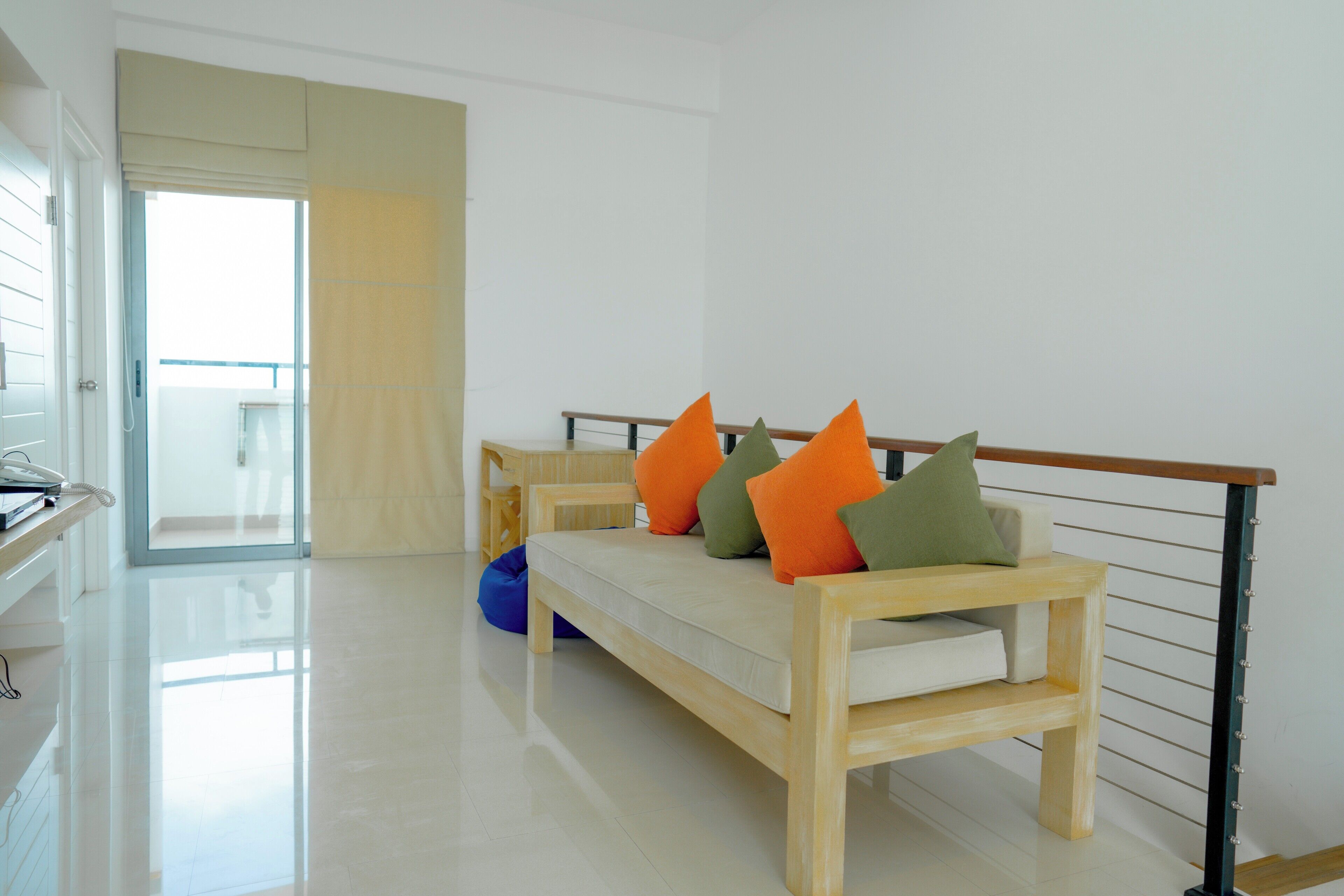 Un salon moderne avec un canapé, des coussins colorés, un banc en bois et un balcon doté d’une balustrade.