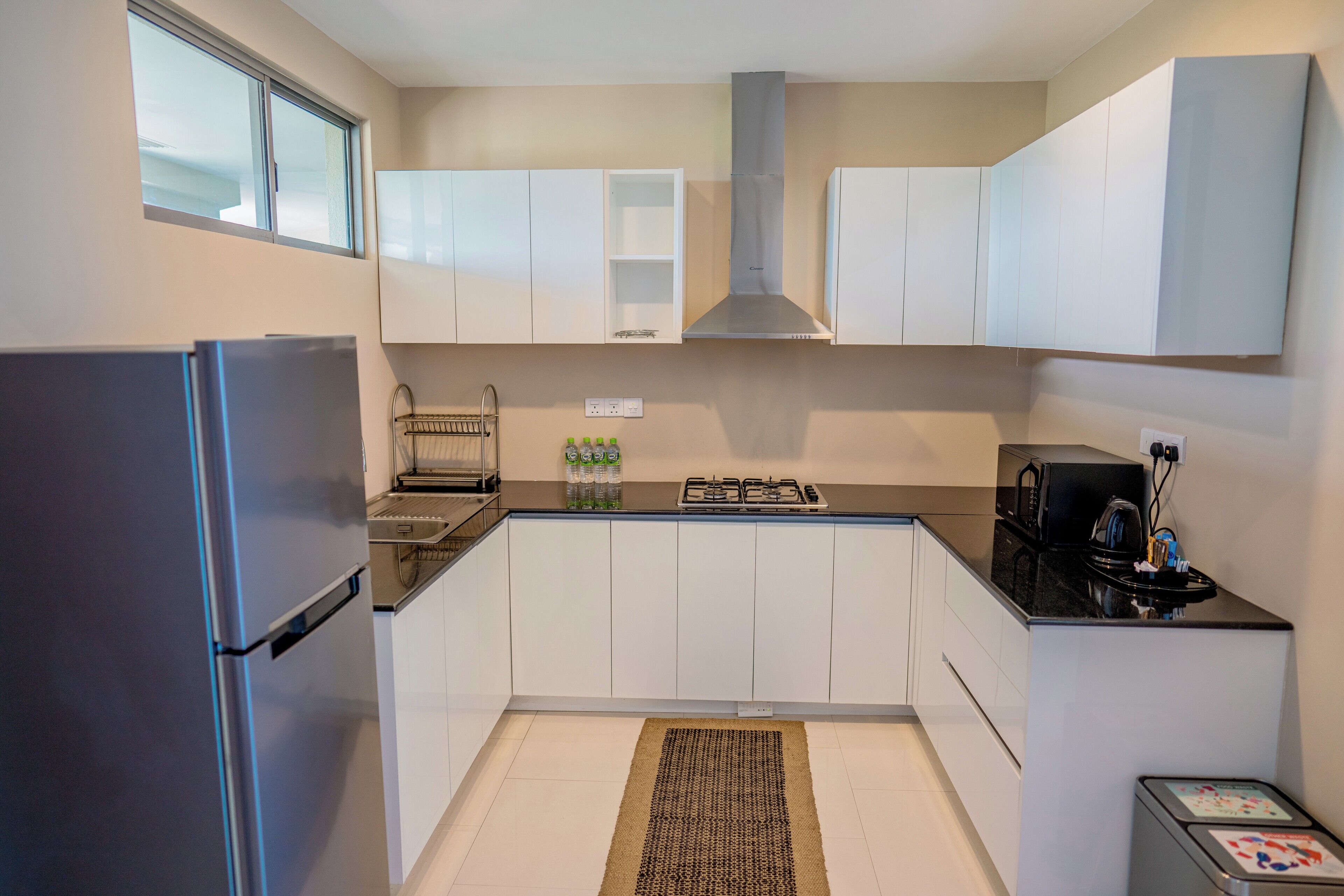 Una cocina compacta con gabinetes blancos, un refrigerador de acero inoxidable, una estufa a gas y un microondas.