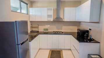 Una cocina compacta con gabinetes blancos, un refrigerador de acero inoxidable, una estufa a gas y un microondas.