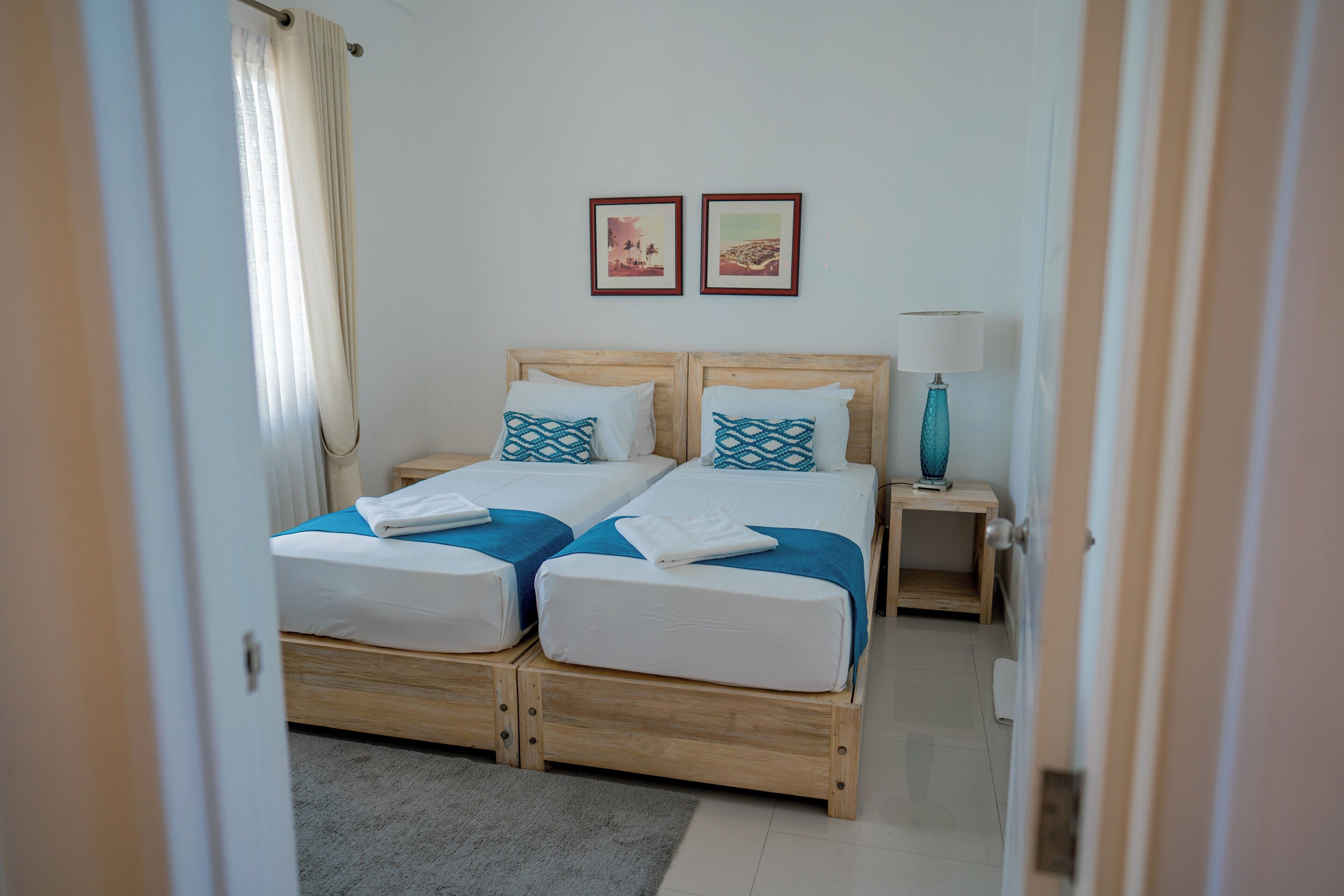 A double bed with two pillows, a nightstand with a lamp, and two framed pictures on the wall.