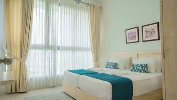 A bedroom with a wooden bed, white bedding, and a teal throw blanket. There are two framed pictures on the wall and a ceiling fan.