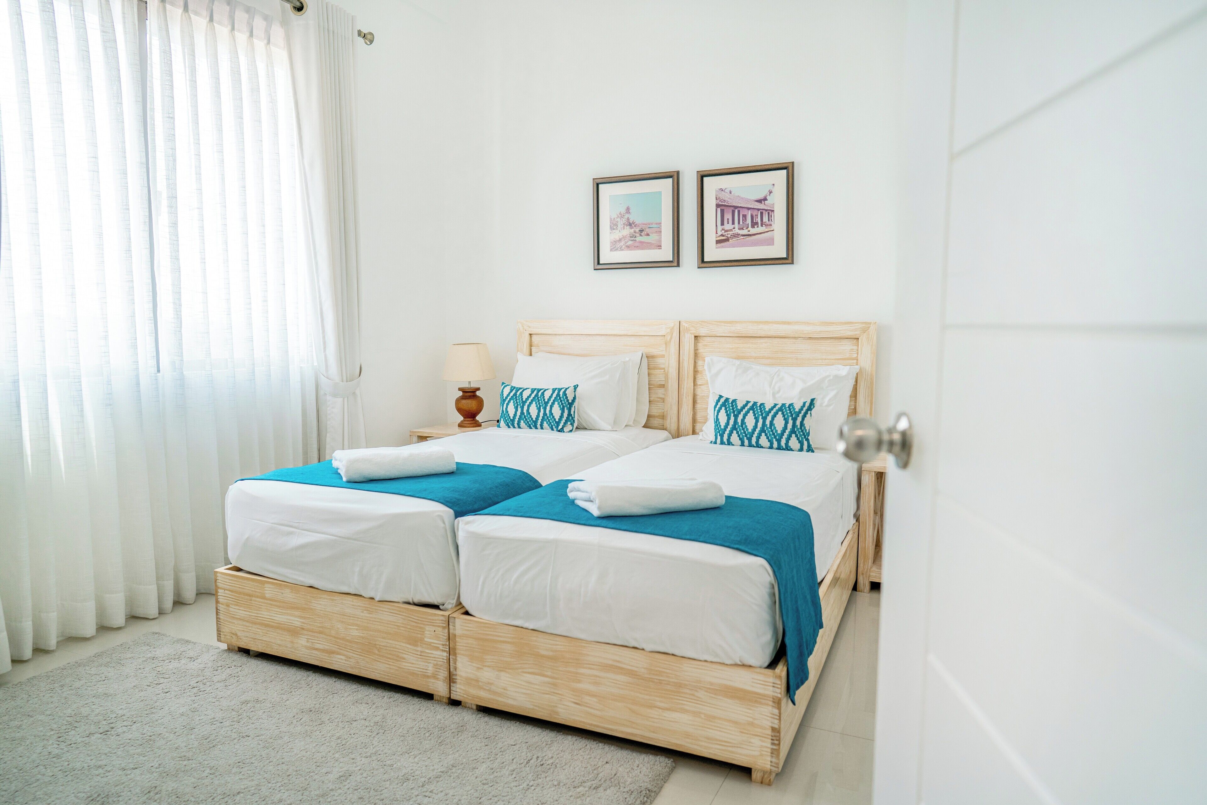 A double bed with white and blue bedding, a bedside table with a lamp, and two framed pictures on the wall.