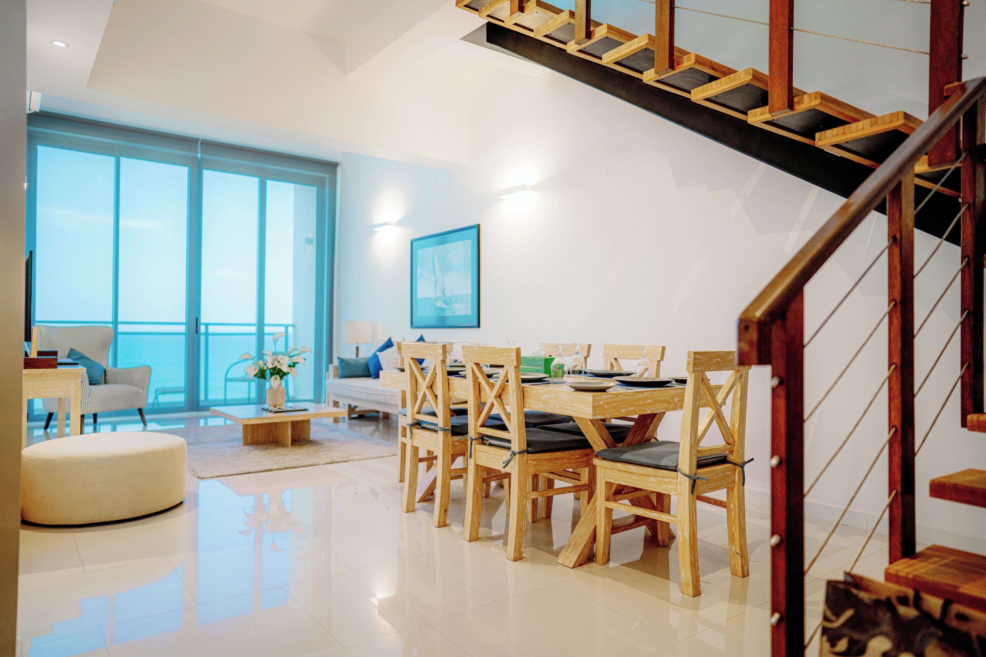 A modern living room with a wooden dining table, chairs, and a staircase.