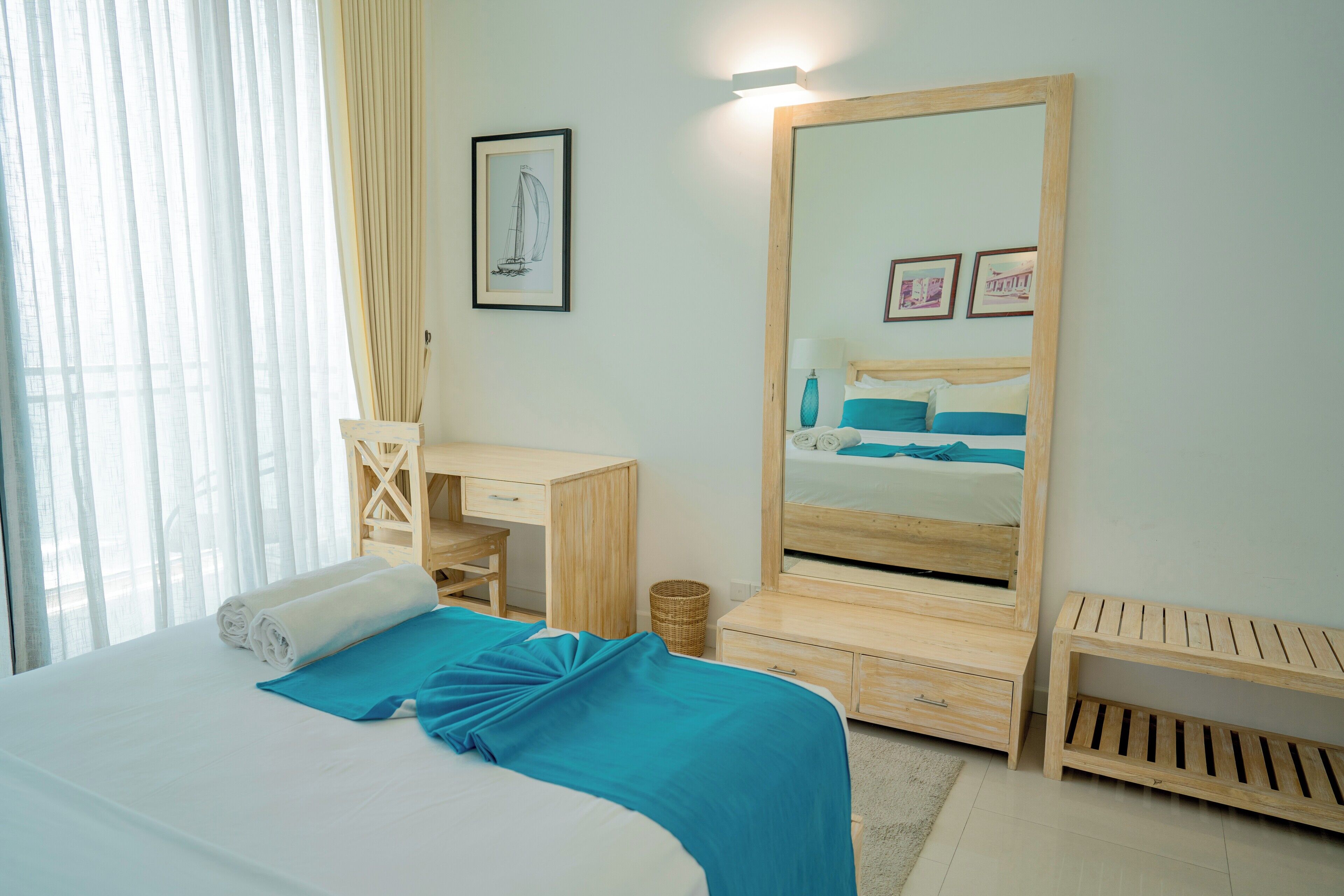 A bedroom with a bed, a desk, a mirror, and a small wooden bench.