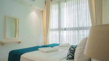 A hotel room with a bed, a bedside table, a mirror, and a window with curtains.