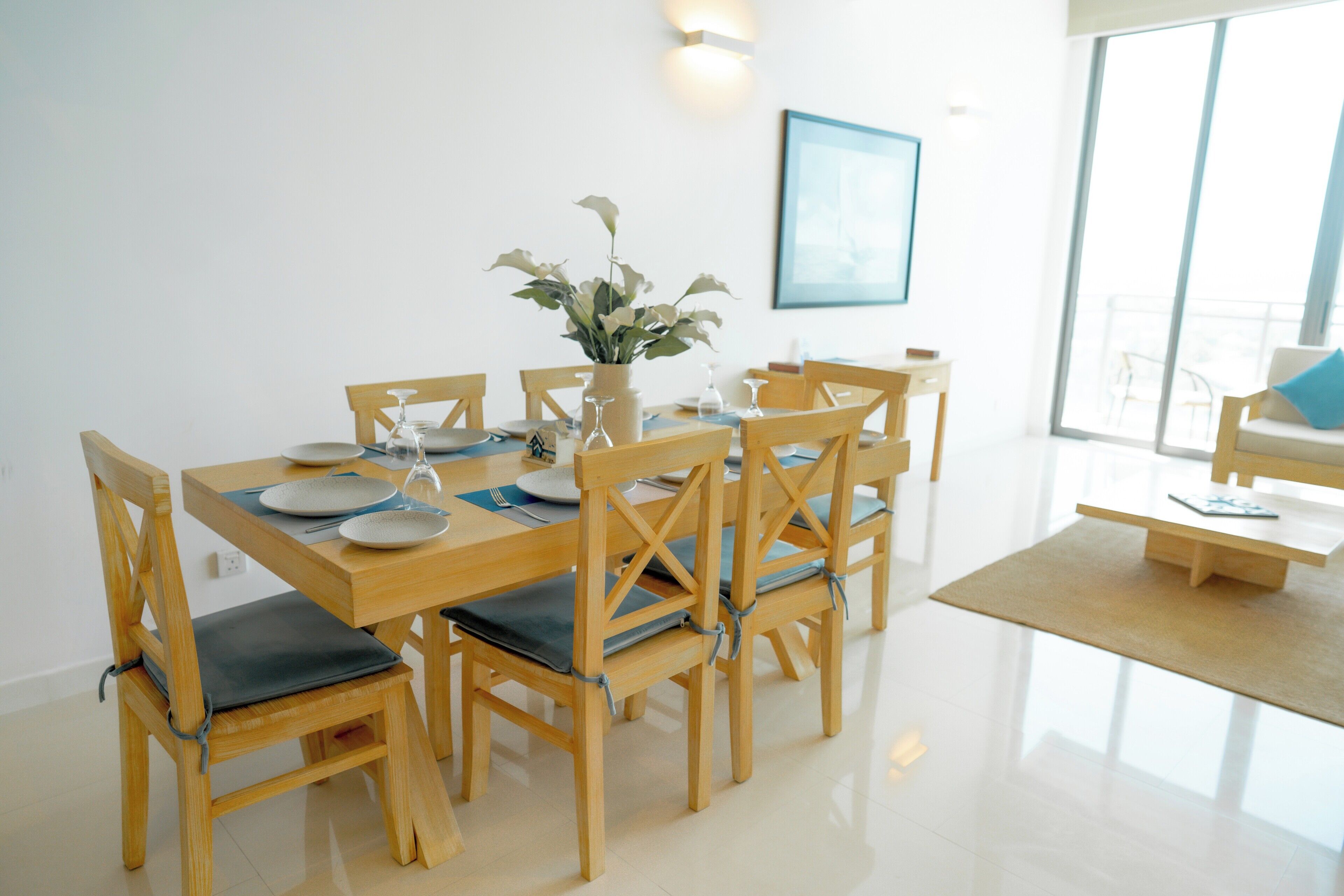 A dining area with a wooden table set for six, surrounded by chairs with blue cushions.